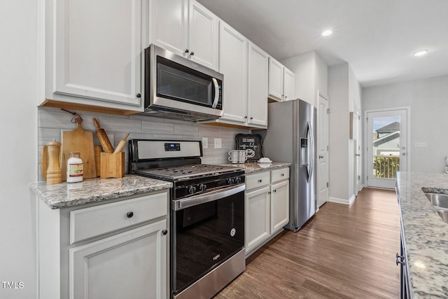 kitchen with backsplash, dark hardwood / wood-style floors, light stone countertops, appliances with stainless steel finishes, and white cabinetry