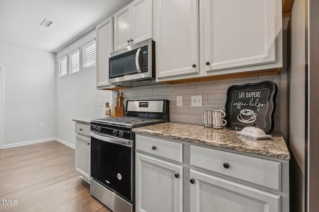 kitchen with white cabinets, light hardwood / wood-style flooring, decorative backsplash, light stone counters, and stainless steel appliances