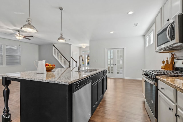 kitchen featuring light hardwood / wood-style flooring, an island with sink, pendant lighting, white cabinets, and appliances with stainless steel finishes