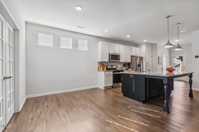 kitchen with stainless steel appliances, dark wood-type flooring, decorative light fixtures, white cabinetry, and an island with sink