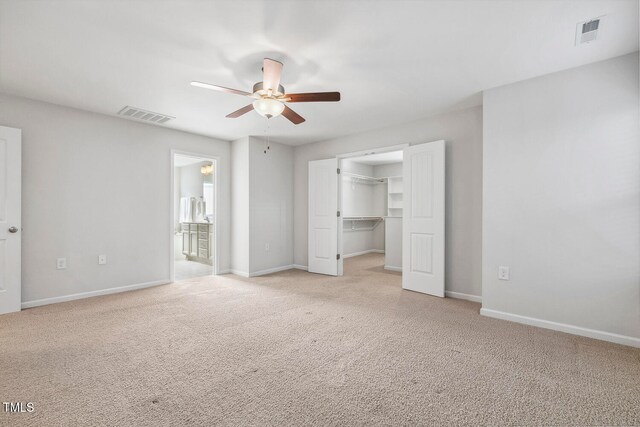 unfurnished bedroom with ceiling fan, a spacious closet, ensuite bathroom, light colored carpet, and a closet