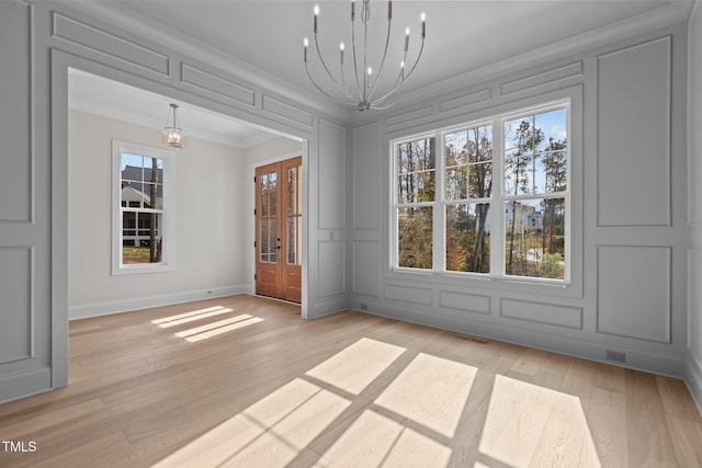 unfurnished dining area with an inviting chandelier, light wood-type flooring, french doors, and crown molding