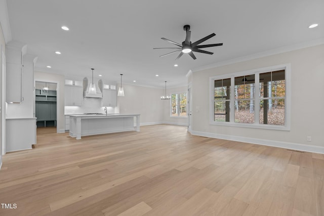 unfurnished living room with light hardwood / wood-style floors, ceiling fan with notable chandelier, a healthy amount of sunlight, and crown molding