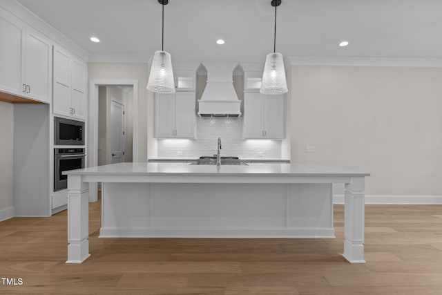 kitchen with a center island with sink, decorative light fixtures, white cabinets, stainless steel oven, and premium range hood