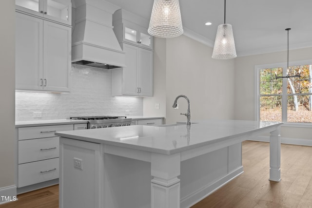 kitchen with hanging light fixtures, custom range hood, a center island with sink, and light hardwood / wood-style flooring