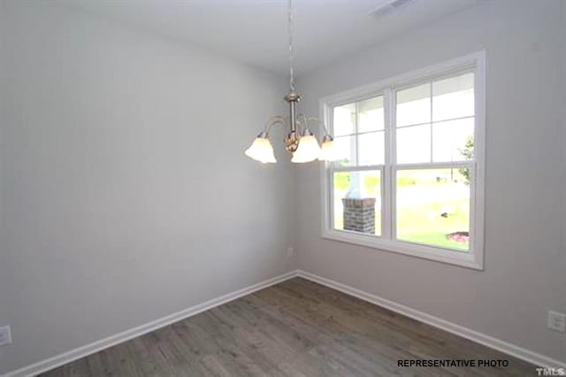 empty room with a chandelier, visible vents, baseboards, and wood finished floors