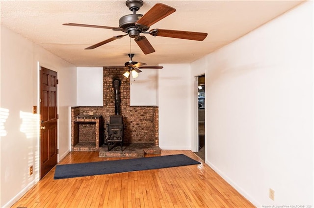 unfurnished living room featuring hardwood / wood-style flooring, a wood stove, and ceiling fan