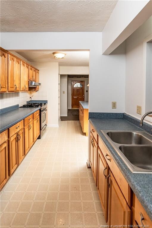 kitchen featuring decorative backsplash, stainless steel gas range oven, sink, and a textured ceiling