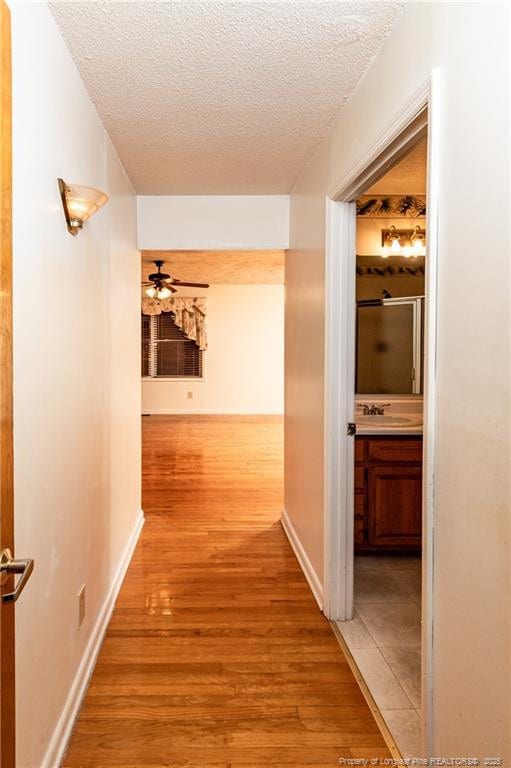 corridor with a textured ceiling, light hardwood / wood-style flooring, and sink