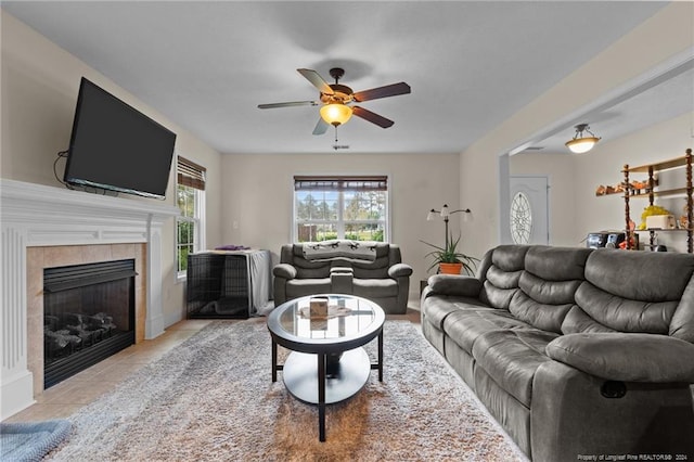 living room with ceiling fan, a tile fireplace, and light tile patterned flooring