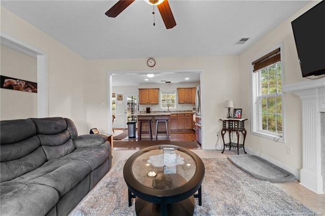 living room with a fireplace, ceiling fan, a healthy amount of sunlight, and light tile patterned floors