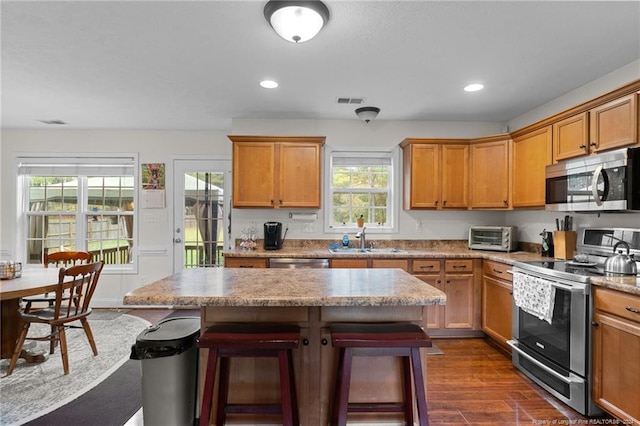 kitchen with stainless steel appliances, a kitchen island, dark hardwood / wood-style floors, sink, and a kitchen breakfast bar