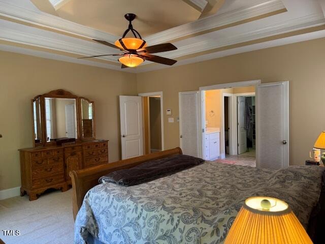 bedroom featuring ceiling fan, a tray ceiling, crown molding, light colored carpet, and connected bathroom