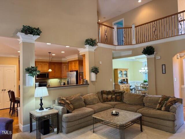 living room featuring ornamental molding, a towering ceiling, ornate columns, a chandelier, and light hardwood / wood-style flooring