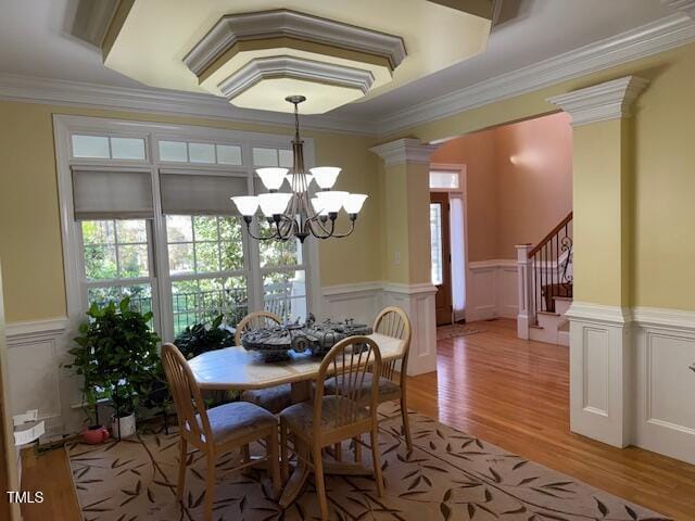 dining area with ornamental molding, ornate columns, a notable chandelier, and light hardwood / wood-style floors