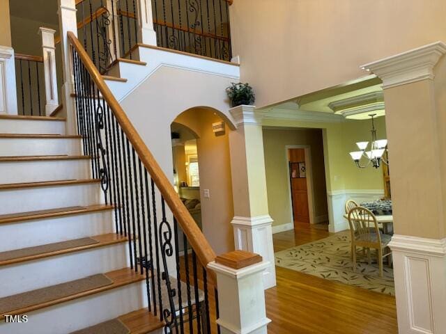 stairs with wood-type flooring, a chandelier, and a high ceiling