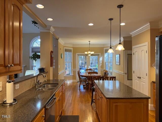 kitchen with ornamental molding, appliances with stainless steel finishes, decorative light fixtures, sink, and light hardwood / wood-style flooring