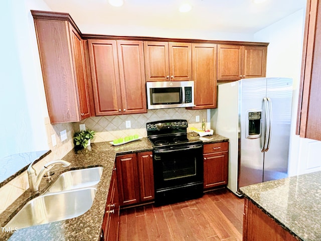 kitchen featuring sink, dark wood-type flooring, stainless steel appliances, backsplash, and dark stone counters