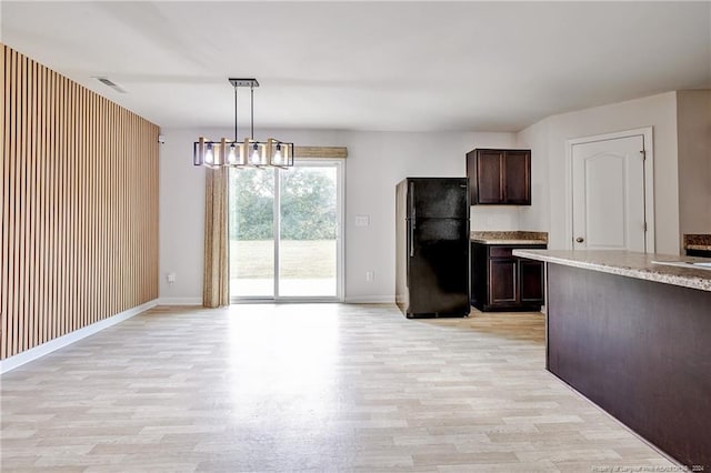 kitchen with pendant lighting, light stone countertops, dark brown cabinets, black refrigerator, and light wood-type flooring