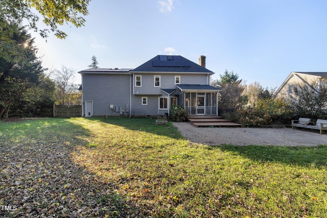 rear view of house with a sunroom, solar panels, and a lawn