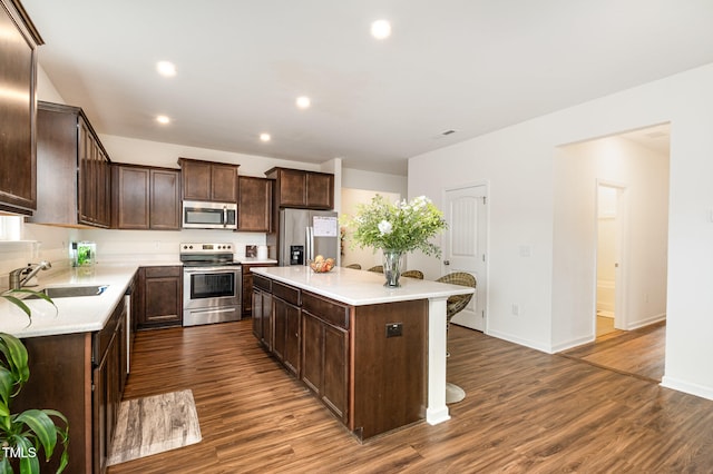 kitchen with dark brown cabinetry, appliances with stainless steel finishes, dark wood-style flooring, a center island, and a sink