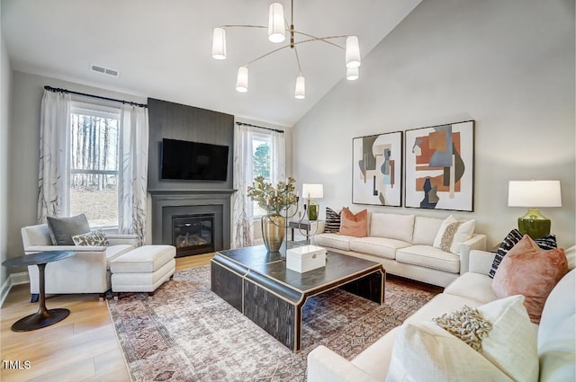 living room featuring high vaulted ceiling, light wood-type flooring, an inviting chandelier, and a fireplace