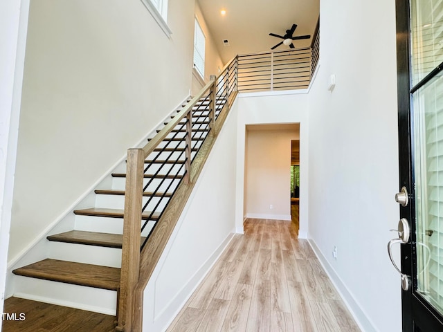 stairway with a high ceiling, wood-type flooring, ceiling fan, and plenty of natural light