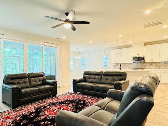 living room with ceiling fan with notable chandelier and light hardwood / wood-style flooring