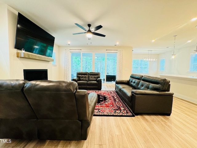 living room with a fireplace, ceiling fan with notable chandelier, and light wood-type flooring