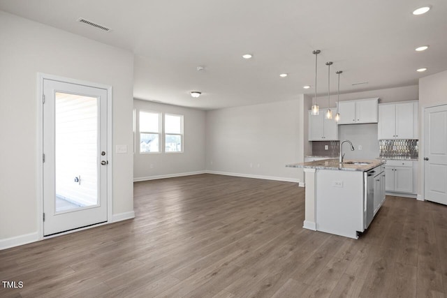 kitchen with hanging light fixtures, sink, backsplash, white cabinetry, and a kitchen island with sink