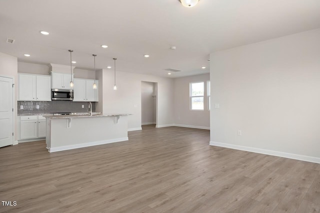 kitchen with white cabinetry, a kitchen island with sink, light hardwood / wood-style flooring, pendant lighting, and a breakfast bar area