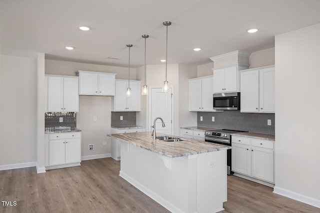 kitchen with appliances with stainless steel finishes, white cabinetry, sink, decorative light fixtures, and a center island with sink