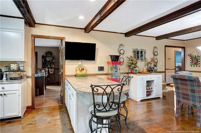 kitchen featuring a breakfast bar area, white cabinets, wood-type flooring, and beam ceiling