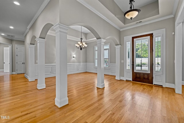 foyer entrance featuring ornamental molding, a raised ceiling, a notable chandelier, ornate columns, and light wood-type flooring