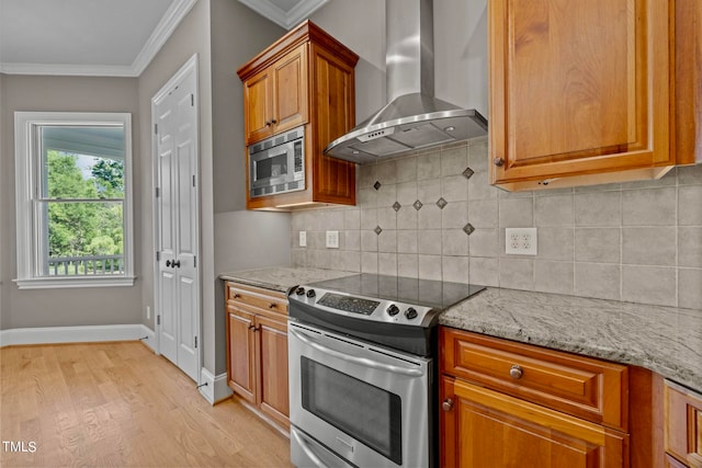 kitchen with light hardwood / wood-style floors, appliances with stainless steel finishes, light stone countertops, crown molding, and wall chimney range hood