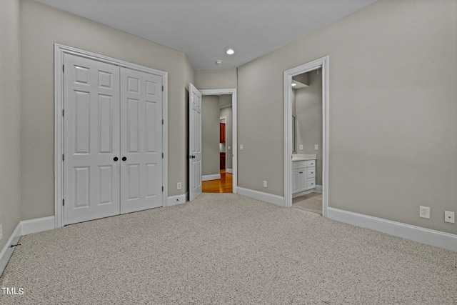 unfurnished bedroom featuring light colored carpet, ensuite bath, and a closet