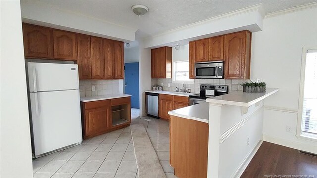 kitchen with stainless steel appliances, kitchen peninsula, light tile patterned floors, ornamental molding, and backsplash