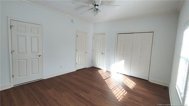 unfurnished bedroom with dark wood-type flooring, ceiling fan, and multiple closets