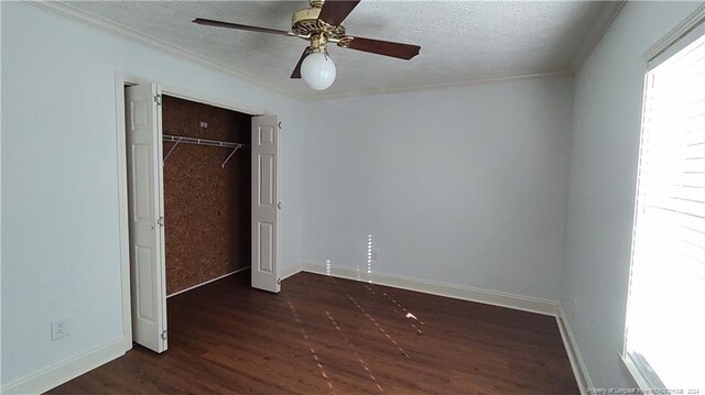 unfurnished bedroom with ceiling fan, a textured ceiling, crown molding, dark wood-type flooring, and a closet