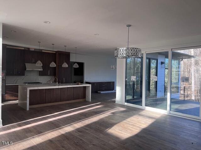 kitchen with dark brown cabinetry, dark hardwood / wood-style flooring, a center island with sink, and backsplash