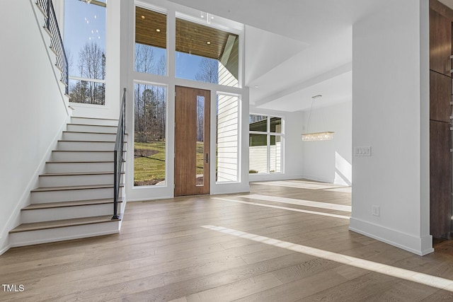 foyer entrance featuring a towering ceiling, a wealth of natural light, a notable chandelier, and light wood-type flooring