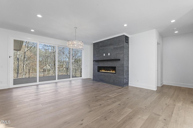 unfurnished living room featuring a tile fireplace, an inviting chandelier, and light hardwood / wood-style flooring