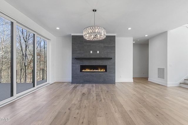 unfurnished living room with a notable chandelier, a fireplace, and light hardwood / wood-style flooring