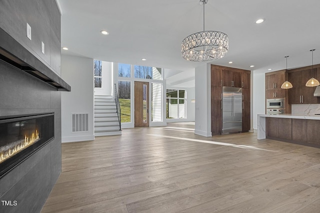 unfurnished living room with a tile fireplace, a chandelier, and light hardwood / wood-style floors