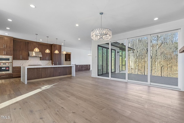 kitchen with stainless steel oven, a notable chandelier, pendant lighting, light hardwood / wood-style floors, and backsplash