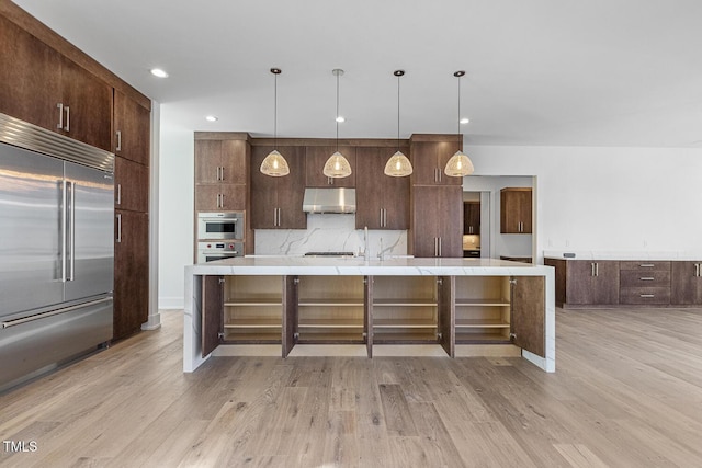 kitchen with built in fridge, decorative light fixtures, tasteful backsplash, an island with sink, and dark brown cabinetry