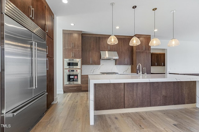 kitchen featuring stainless steel appliances, decorative light fixtures, a kitchen island with sink, and decorative backsplash