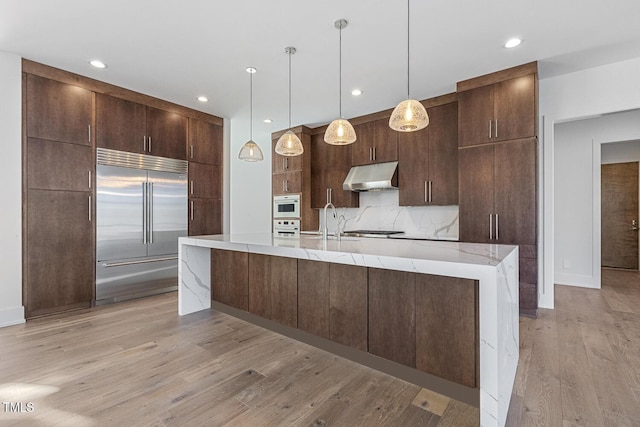 kitchen featuring stainless steel appliances, tasteful backsplash, pendant lighting, and an island with sink