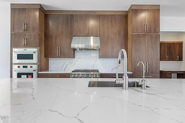 kitchen with sink, tasteful backsplash, light stone counters, stainless steel appliances, and exhaust hood