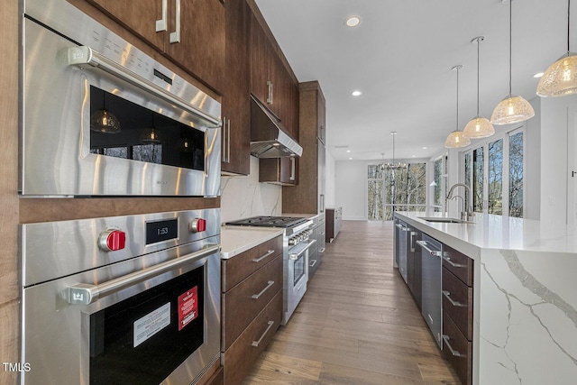 kitchen featuring sink, stainless steel appliances, light stone counters, tasteful backsplash, and decorative light fixtures